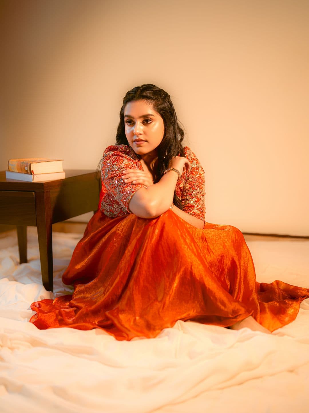 Woman seated in an orange lehenga skirt and red embroidered choli with gold work